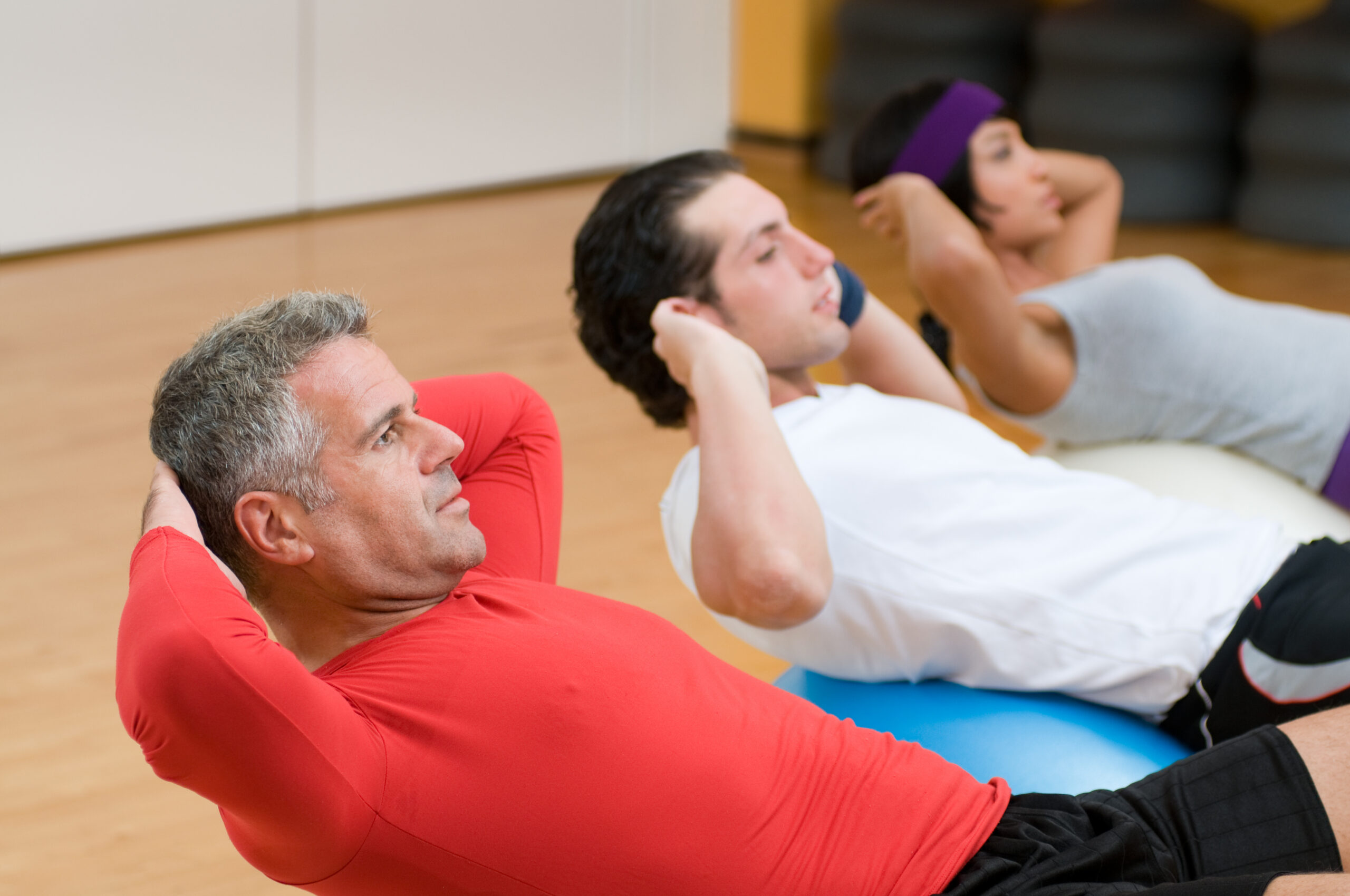 Healthy people with mature instructor doing sit-ups on fitness ball at gym