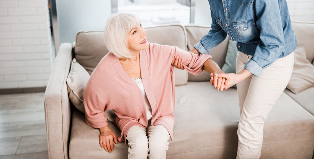 Smiling girl holding hand of elderly woman and helping her to stand up stock photo