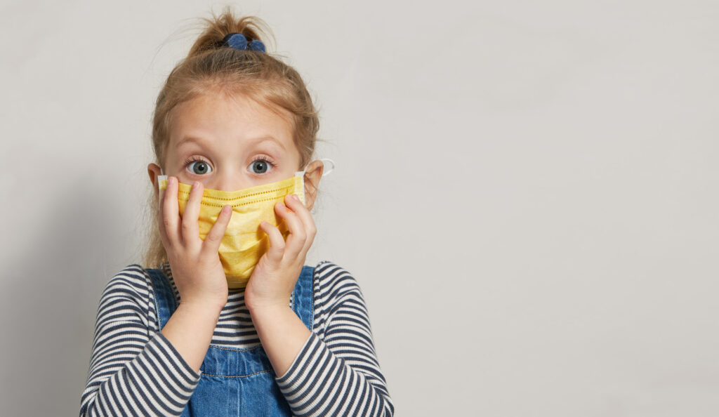 Sick and surprised little girl child in a protective medical mask holds hands near the face. The concept of global quarantine during the coronavirus pandemic