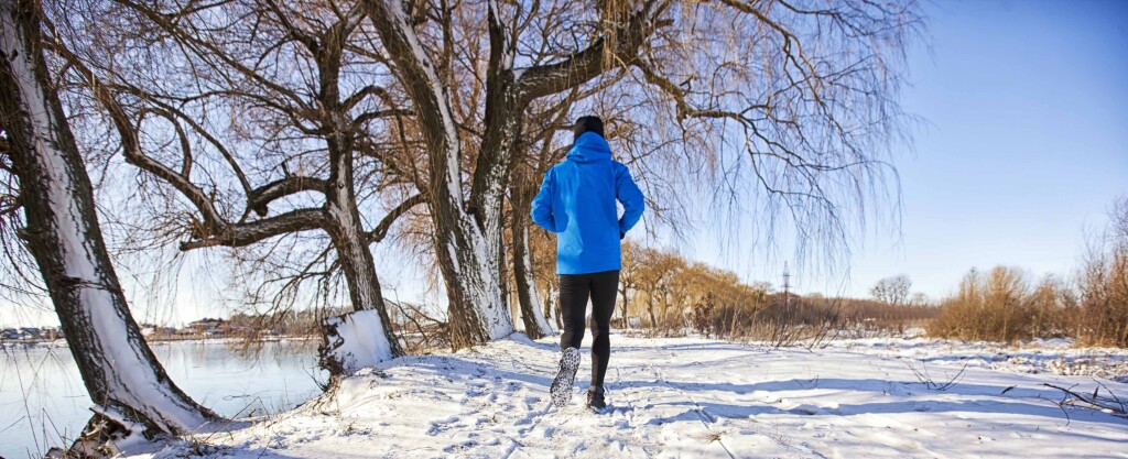 The man in sportswear is jogging through the winter country roads covered by snow